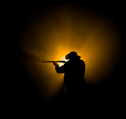 Dark, foggy outdoor silhouette of a cowbow shooting a level-action Winchester 94 rifle.