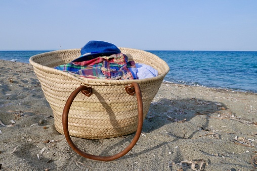 Straw bag filled with clothes on a deserted beach.