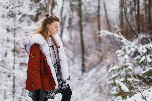 Redhead woman in red jacket with fur in winter forest. Pretty woman enjoying vacation. Girl in nature. Feel happiness. Frost on trees