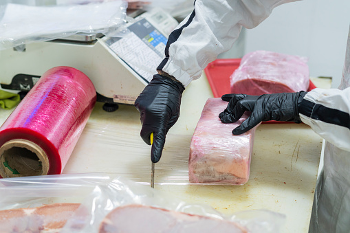 Hispanic man, average 30 years old, dressed in a white anti-fluid uniform, a butcher shop employee places a tray with several bags of meat on the scale in order to obtain its weight