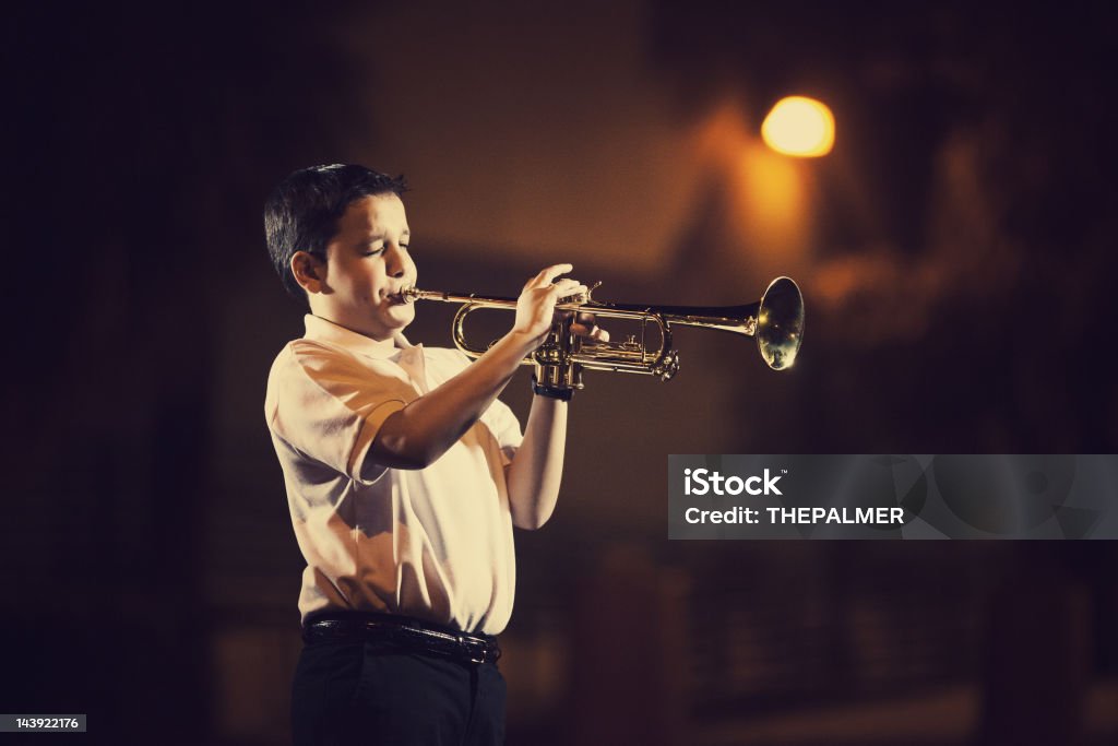 eleven years old kid playing the trumpet eleven years old kid playing the trumpet outdoors with a spotlight from a street lamp in the back Child Stock Photo