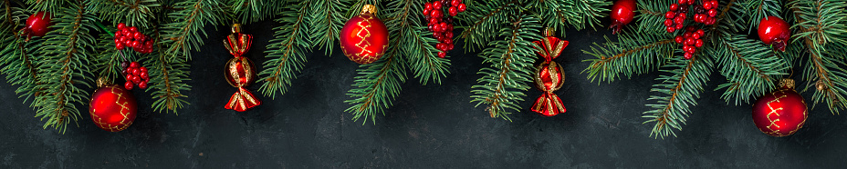 Christmas dark grunge horizontal background, top view. Fir twigs, red golden berries, baubles. Winter holidays, New Year decoration, pine tree branches, snow covered cones, flat lay, copy space.