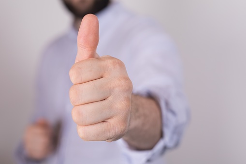 A closeup of a person doing the thumbs-up gesture under the lights on a blurry background