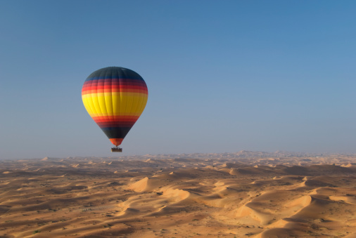 Luxor, Egypt, April 15, 2023: A hot air balloon with tourists floats over the Valley of the Kings near the Nile River at dawn.
