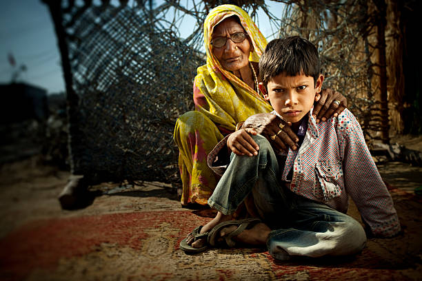 sorriso escarninho pouco indian menino sentado no chão com seu grandmothe - india slum poverty family - fotografias e filmes do acervo