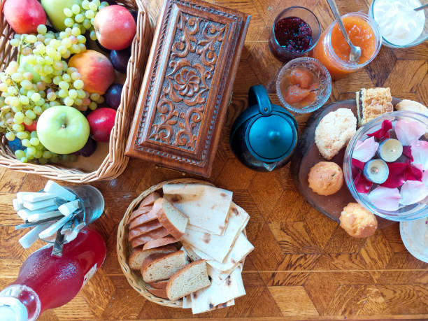 A prepared table for a romantic breakfast for two. Small candles and rose petals float in a vade in a glass bowl. Ladies food pancakes and fruits.