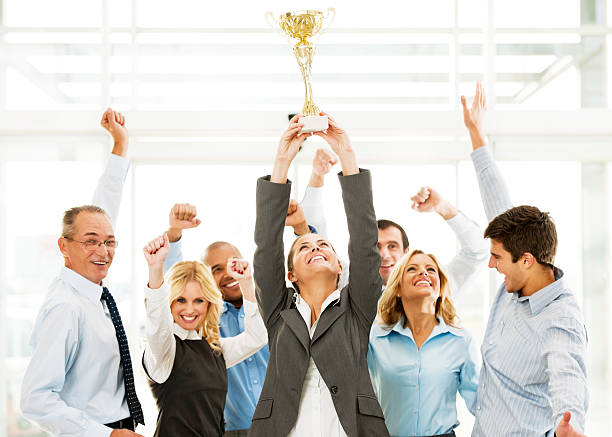 Cheerful group of businesspeople winning the cup with hands up. Successful businesspeople celebrating with the cup in hands.    office competition stock pictures, royalty-free photos & images
