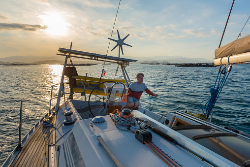 sailor steering sailboat at sunset, twilight time on the open sea