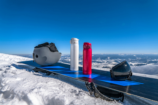 Ski helmet, two thermo bottles and ski goggle on snowboard on snowy mountain top
