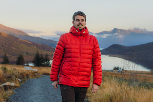 Happy male in a red jacket admiring the autumn in the mountains and walking on the footpath during twilight in More og Romsdal county