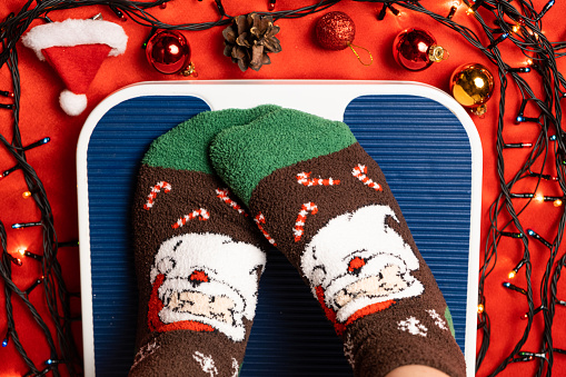 Una mujer con calcetines navideños se para en la balanza, se pesa después de la gula durante las vacaciones photo
