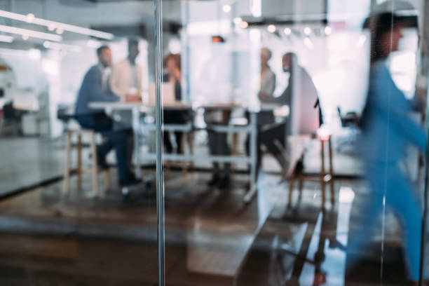 Defocused shot of group of business persons in business meeting. Group of entrepreneurs on meeting in board room. Corporate business team on meeting in the office. The view is through glass.