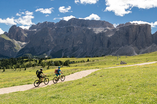 Two male mountainbikers are riding on a gravel footpath in front of a scenic rockface in the Dolomites area in Italy.\nCanon EOS 760D, 1/800, f/7,1 , 18 mm.