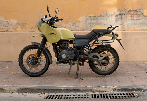 Barcelona, Spain - October 23, 2022: A Royal Enfield Himalayan motorcycle with a knobby wheel and mud, parked on the curb