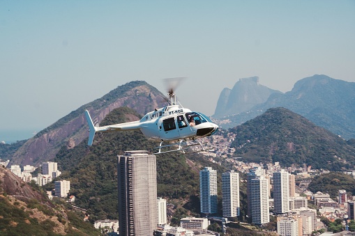 Rio de Jnaeiro, Brazil – August 27, 2006: A white Bell Jet Ranger helicopter flying with Rio de Janeiro cityscape buildings, mountains, and blue sky in the background, same level point of view