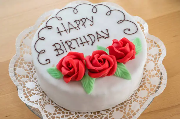 weiße Torte mit Aufschrift Happy Birthday und roten Marzipanrosen