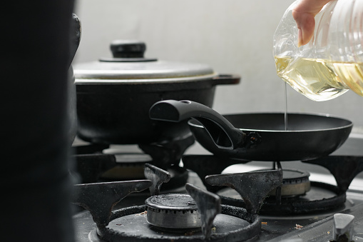 girl pouring the oil into the frying pan, which is on top of a burner, on a gas stove, preparing the typical Colombian breakfast.