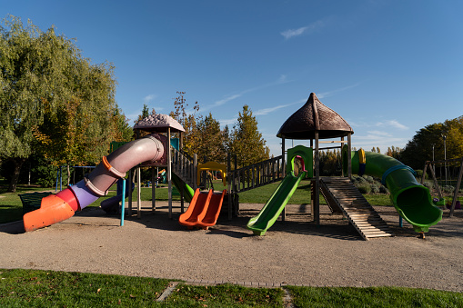 Multi-ethnic group of elementary age school children playing on a school or park playground in spring or summer season.  A teacher or parent is with the children.