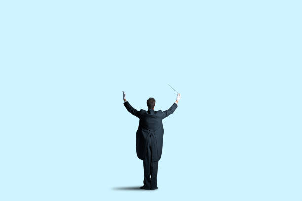 Rear View Of Music Conductor On A Blue Background A rear view of a music conductor wearing a tuxedo and tails as he is prompting his orchestra to commence the music. musical conductor stock pictures, royalty-free photos & images