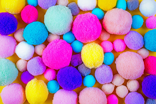Many colorful pom-poms felt balls of different sizes lie on a yellow background.