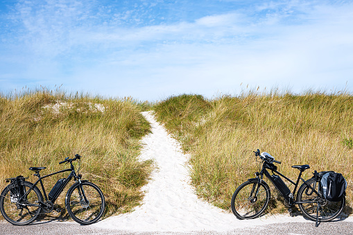 Two black electric bicycles on a dike with a path to the sandy beach on the Baltic Sea coast.