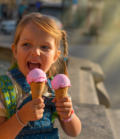 Portrait of Cute and happy four years old girl with two ice creams outside.