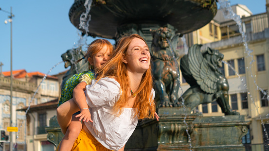 Lovely red haired mother and little daughter playing, having fun moments near the fountain in the old European town.