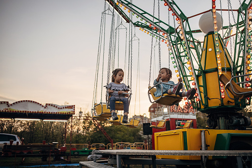 Two girls, cute little sisters riding together on a carousel in amusement park.