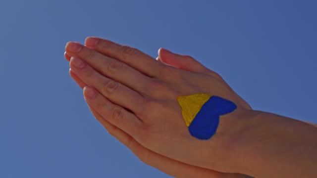 female hands in pray painted in Ukraine flag colors