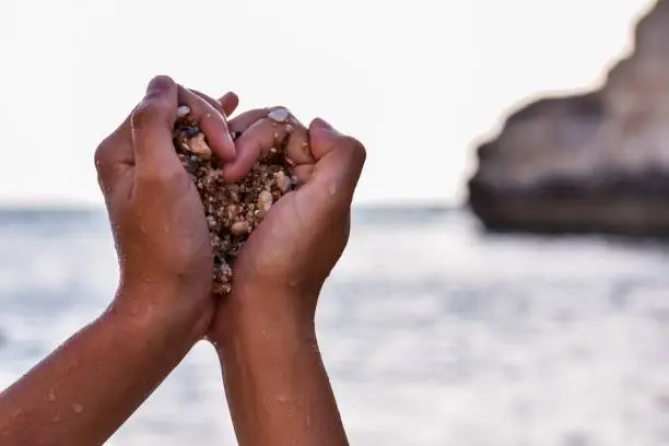 Photo of Hands of a black person grabbing stones in the shape of a heart