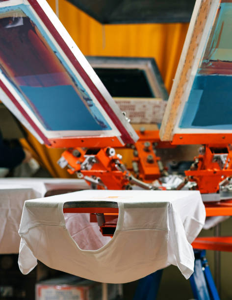 weißes t-shirt ist druckfertig. erstellen eines drucks auf t-shirt im workshop. siebdruckproduktion. siebdruck vertikales foto mit selektivem fokus - serigraphy stock-fotos und bilder