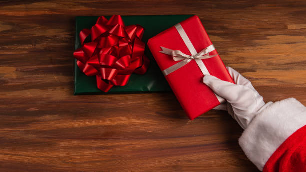 Santa holding a red box present with a silver bow on over a wood backdrop with copy space