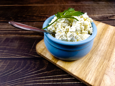 A blue cup with homemade cottage cheese on a kitchen board and a dark table made of boards. The concept of home-made healthy food.