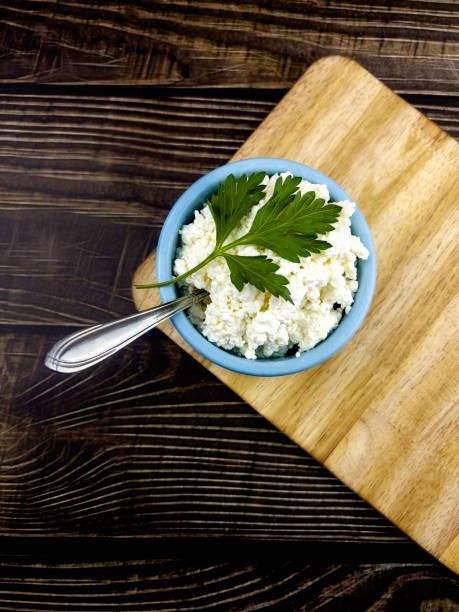 A blue cup with homemade cottage cheese on a kitchen board and a dark table made of boards.