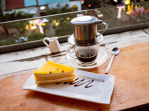 Glass of Vietnamese coffee with a filter and a lemon cake on a wooden table