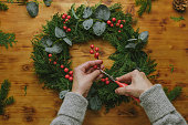 Hands decorates Christmas wreath with holly berries.