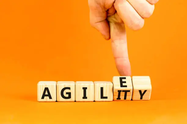 Agile and agility symbol. Concept words Agile and Agility on wooden cubes. Beautiful orange table orange background. Businessman hand. Business agile and agility concept. Copy space.