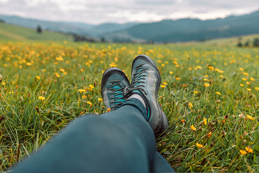 View on feet wearing hiking boots on the top of the mountain against the background of a green hills.
