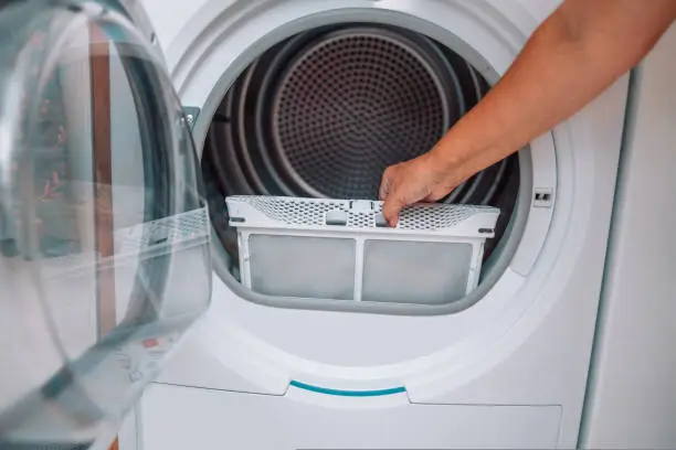 Housewife cleanup lints and dirt from tumble dryer filter. Clothes dryer lint filter that is covered with lint. Taking the lint out from dirty air filter of the dryer machine before use the machine.