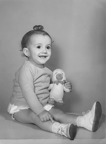 Black and White Image taken in the 60s, little girl posing holding a phone looking away holding a toy