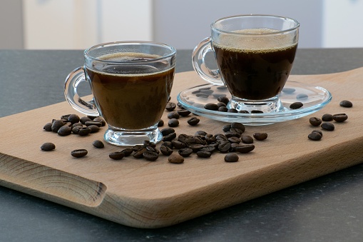 A couple of cups of coffee drinks in clear cups and beans spilled on a wooden board