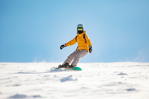 Young adult woman snowboarding in mountains at ski resort