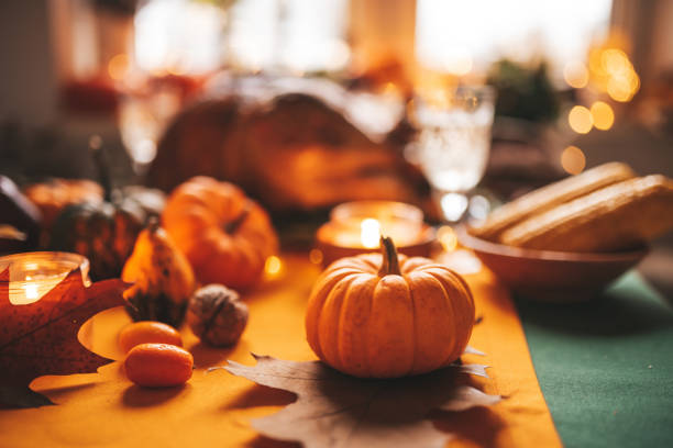 Classic USA Thanksgiving day dinner with holiday autumn decor and candles. Family dining room table set with delicious golden roasted turkey on platter garnished rosemary and fresh small pumpkins