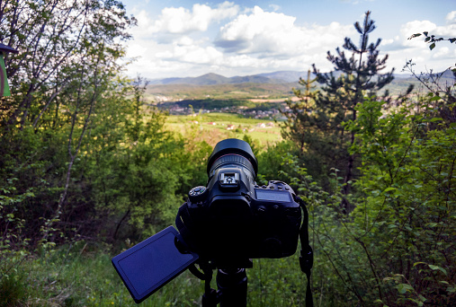 A camera on a tripod standing between trees shooting landscape