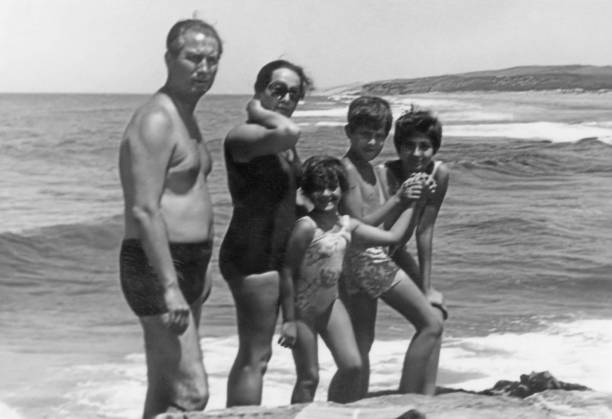 imagem em preto e branco tirada nos anos 60: casal maduro com seus três filhos na praia - old fashioned swimwear couple retro revival - fotografias e filmes do acervo