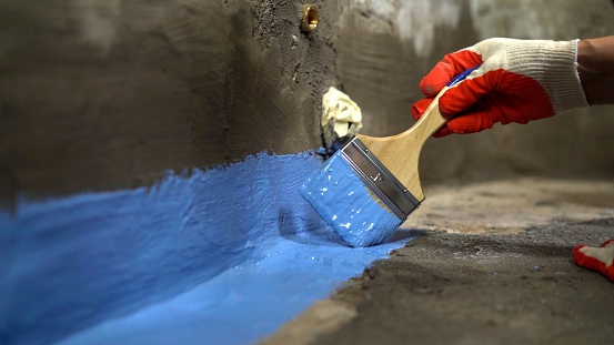 Waterproofing the floor with a brush.Waterproofing concrete mortar. The master puts waterproofing on a concrete floor with a brush. Bathroom floor waterproofing.
