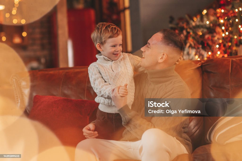 Candid authentic happy dad playing with little son fooling around at wooden lodge Xmas decorated Smile little boy and dad having fun with each other hugs and kisses indoor waiting santa. Celebrating New year with garlands lights of Noel tree winter season Xmas spirit eve 25 December paternal love Christmas Stock Photo Candid authentic happy dad playing with little son fooling around at wooden lodge Xmas decorated Smile little boy and dad having fun with each other hugs and kisses indoor waiting santa. Celebrating New year with garlands lights of Noel tree winter season Xmas spirit eve 25 December paternal love Christmas Stock Photo