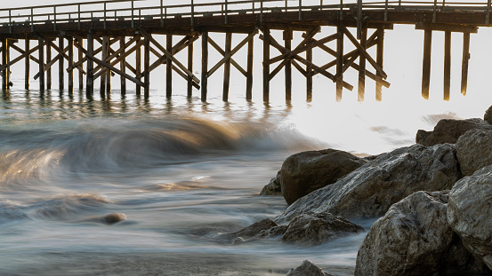 A wave is forming and crashing against rocks at Goleta Beach in Santa Barbara. Goleta Pier is pictured in the background.