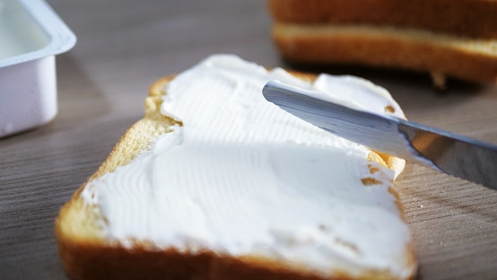 Knife spreading butter on a piece of bread, close up view. Breakfast or lunch concept.