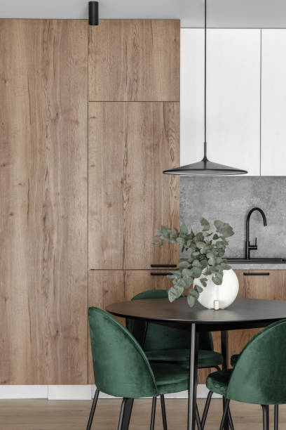 istock Modern minimalistic kitchen and dining room interior with wooden and white surfaces, green chairs and eucalyptus in ceramic vase. Aesthetic simple interior design concept. 1439298319